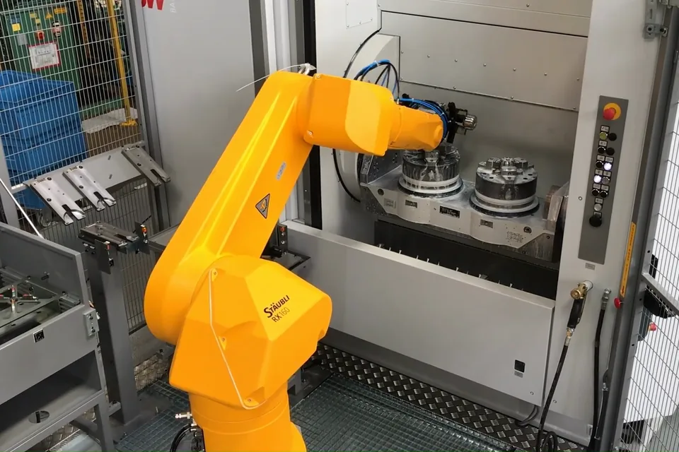Robot Stäubli RX160 orange chargeant une machine-outil : deux mandrins sur la table de la machine.