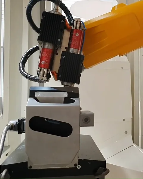 Robot Stäubli orange équipé d’une broche d’usinage, au-dessus d’un poste de travail.